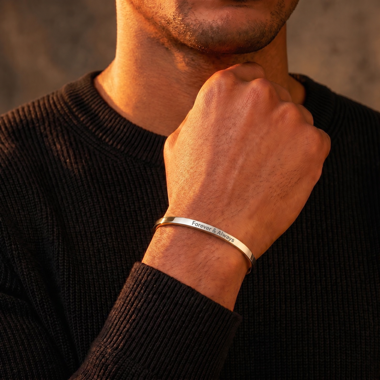 A close-up of a man wearing a thin silver metal cuff bracelet on his wrist, with his hand resting near his neck. The bracelet is engraved with the words 'Forever & Always'.