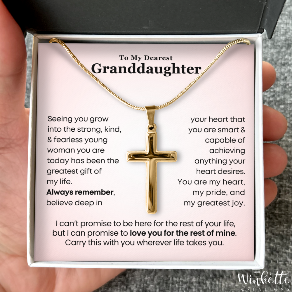 Gold cross necklace in a box with a message for a granddaughter, held by a hand. Gift from grandma or grandpa
