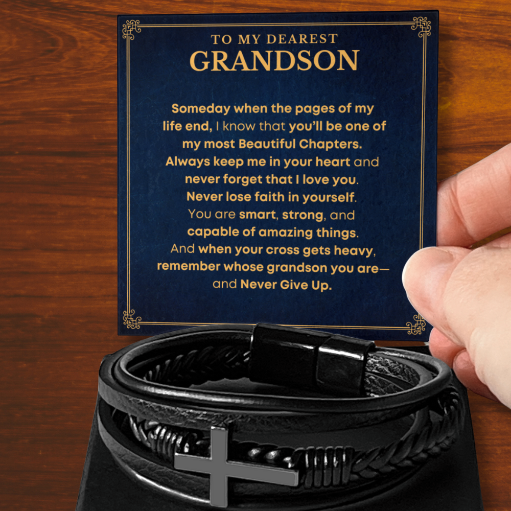 Hand holding a message card that reads “To My Dearest Grandson – Never Lose Faith,” paired with a black leather cross bracelet on display. The heartfelt card features a gold and navy blue design, making it a meaningful gift for grandson from Grandma.