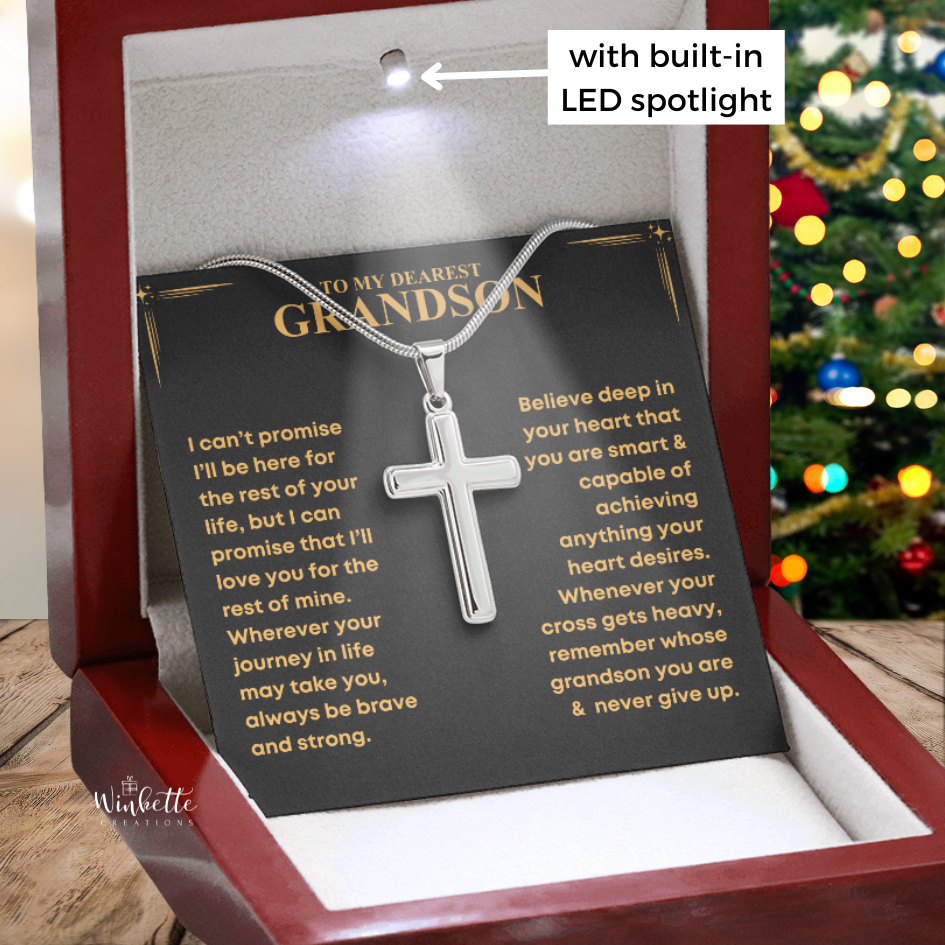 Silver cross necklace on a card with text, displayed in a red box with LED lighting, Christmas tree in the background. Gift for grandson