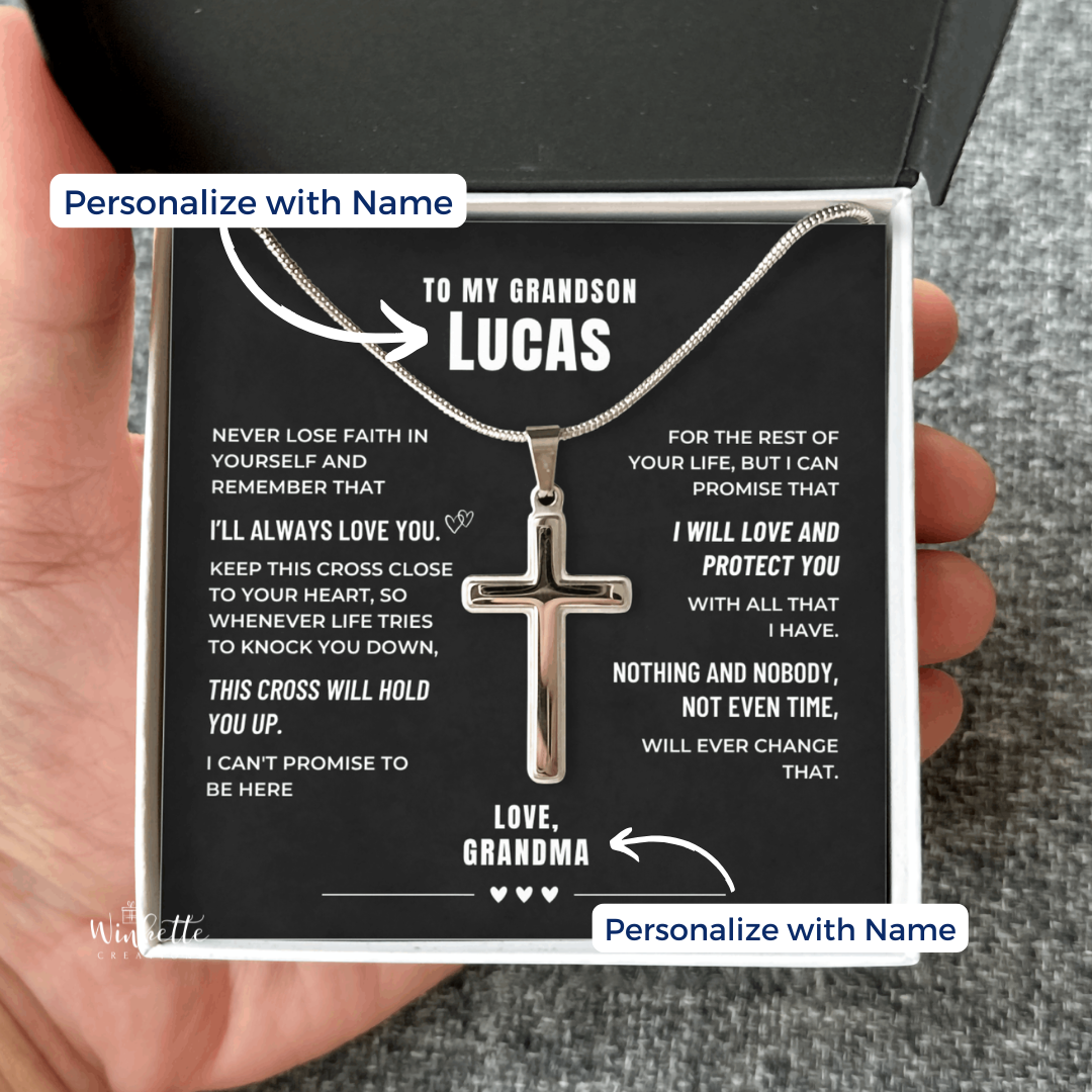 A hand holds an open gift box containing a cross necklace for a grandson with a heartfelt personalized  message card from Grandma. The necklace is displayed on a black card with white text that reads 'TO MY GRANDSON LUCAS' and includes customizable name placeholders.