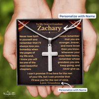 Thumbnail for A silver cross necklace on a chain presented in a square gift box with a personalized memorial message for a grandson. Two hands hold the box against a blurred green outdoor background.