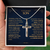 Thumbnail for A silver cross pendant necklace displayed inside an open gift box with a dark navy message card addressed to a son, held in a person's hand.