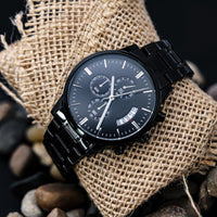 Thumbnail for Black wristwatch with detailed face on a textured fabric background