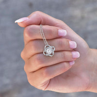 Thumbnail for Close-up of silver love knot necklace pendant with cubic zirconia crystals held in hand – gift for granddaughter.