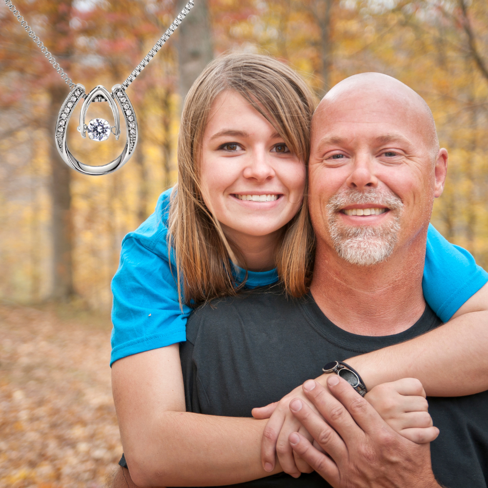 Daughter embracing her dad outdoors with a horseshoe necklace.