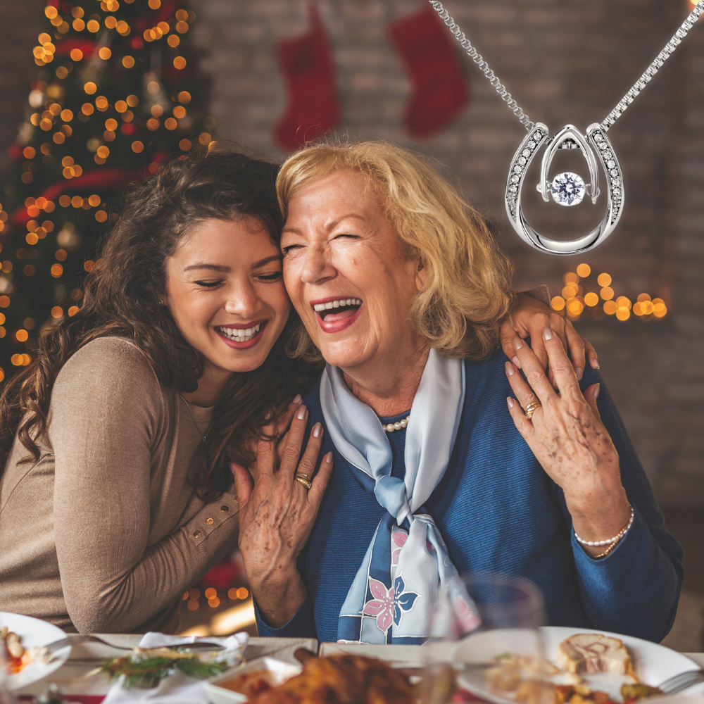 Mom and daughter laughing together with a Christmas tree and stockings in the background, featuring a silver necklace with a horseshoe pendant.
