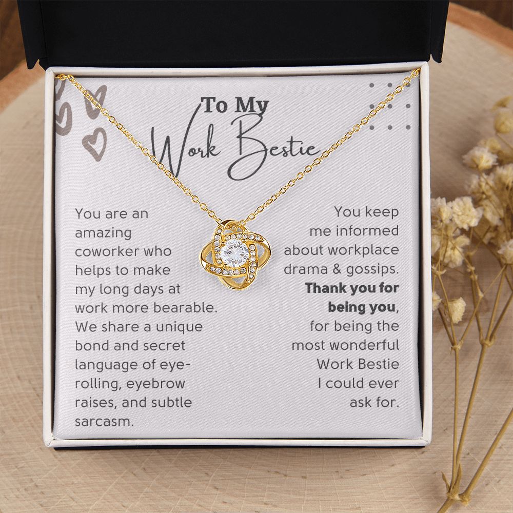A gold-colored necklace with a Love Knot design, presented in a box with a message for a work bestie.